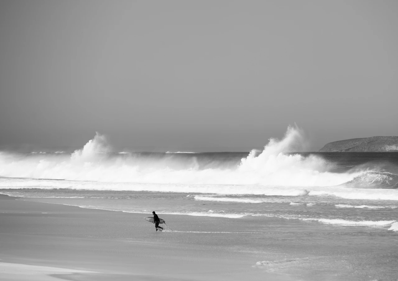 surfer runs up the beach black and white